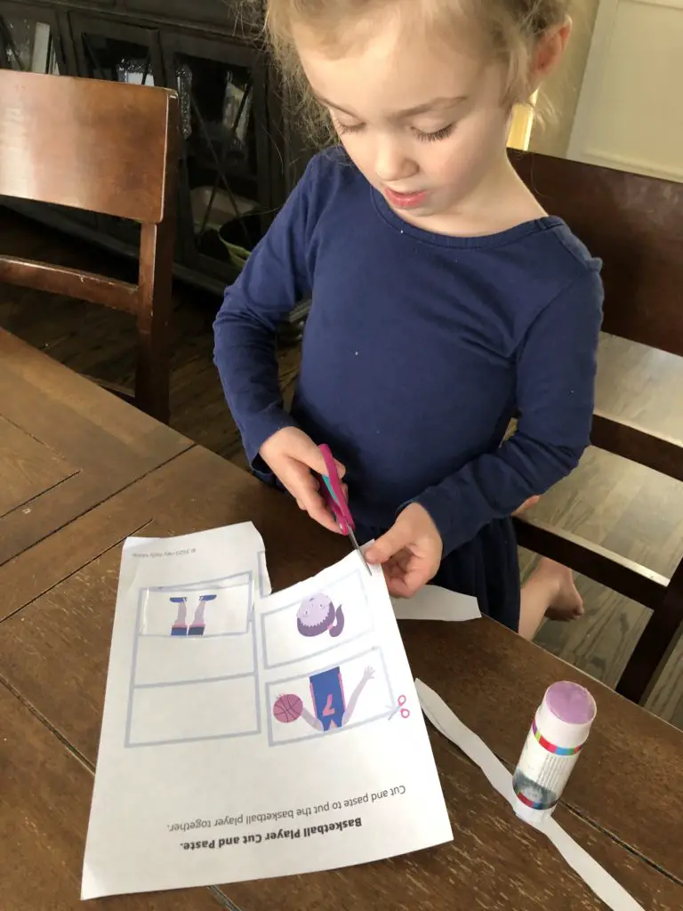 Daughter holding scissors correctly and working on free preschool cutting workbook page